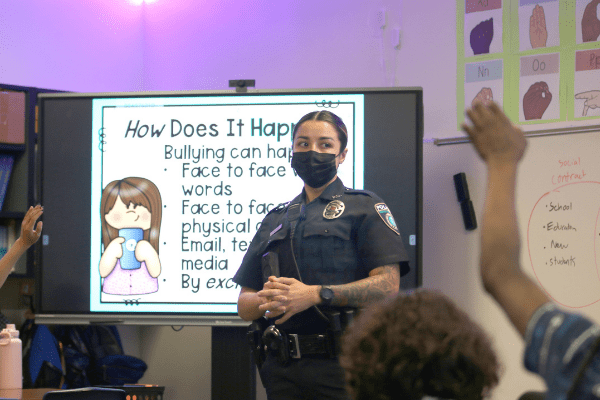 Officer Alvear in classroom with anti-bullying message on projection screen.